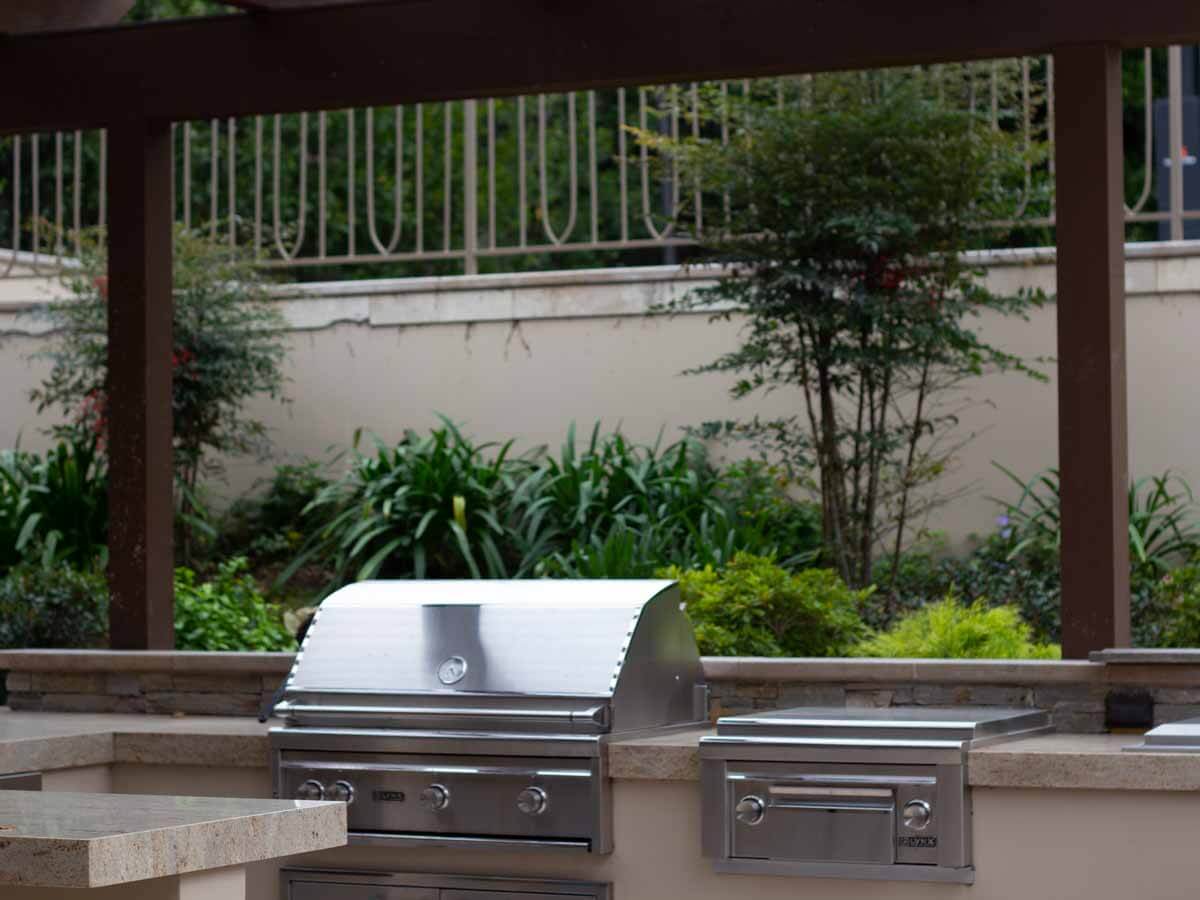Twin stainless grills in a stone counter under a wood pergola