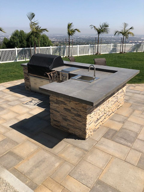 Stacked stone BBQ island with concrete counter on a paver deck overlooking the city