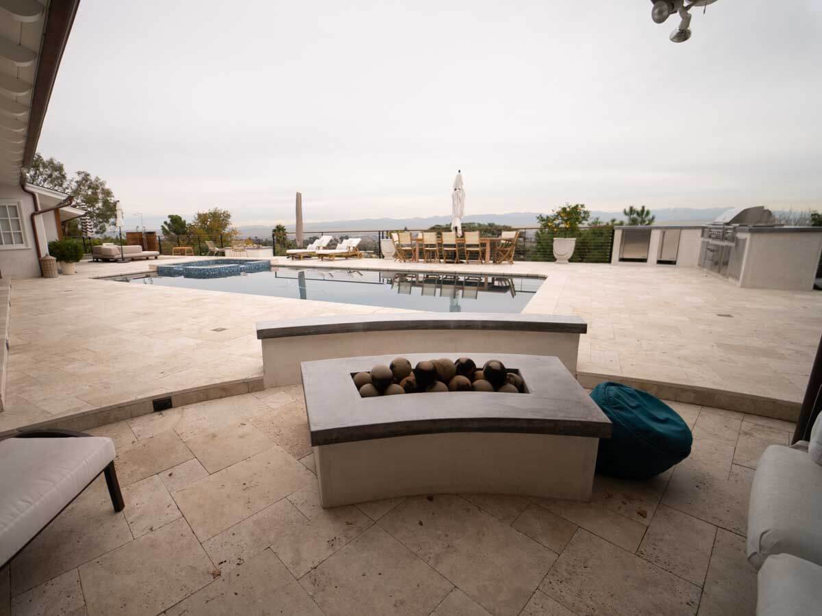 Curved concrete bench and fire pit beside a resort-style pool at dusk