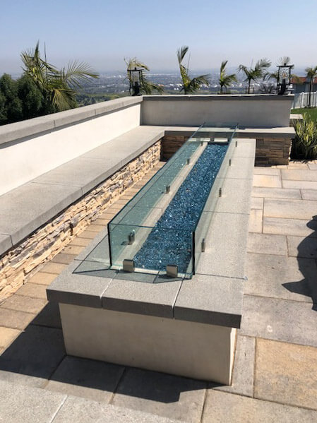 Long linear fire feature with a glass windscreen on a stone terrace
