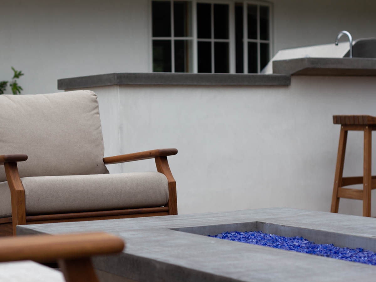 Modern gray concrete fire table with blue fire glass and wood armchairs