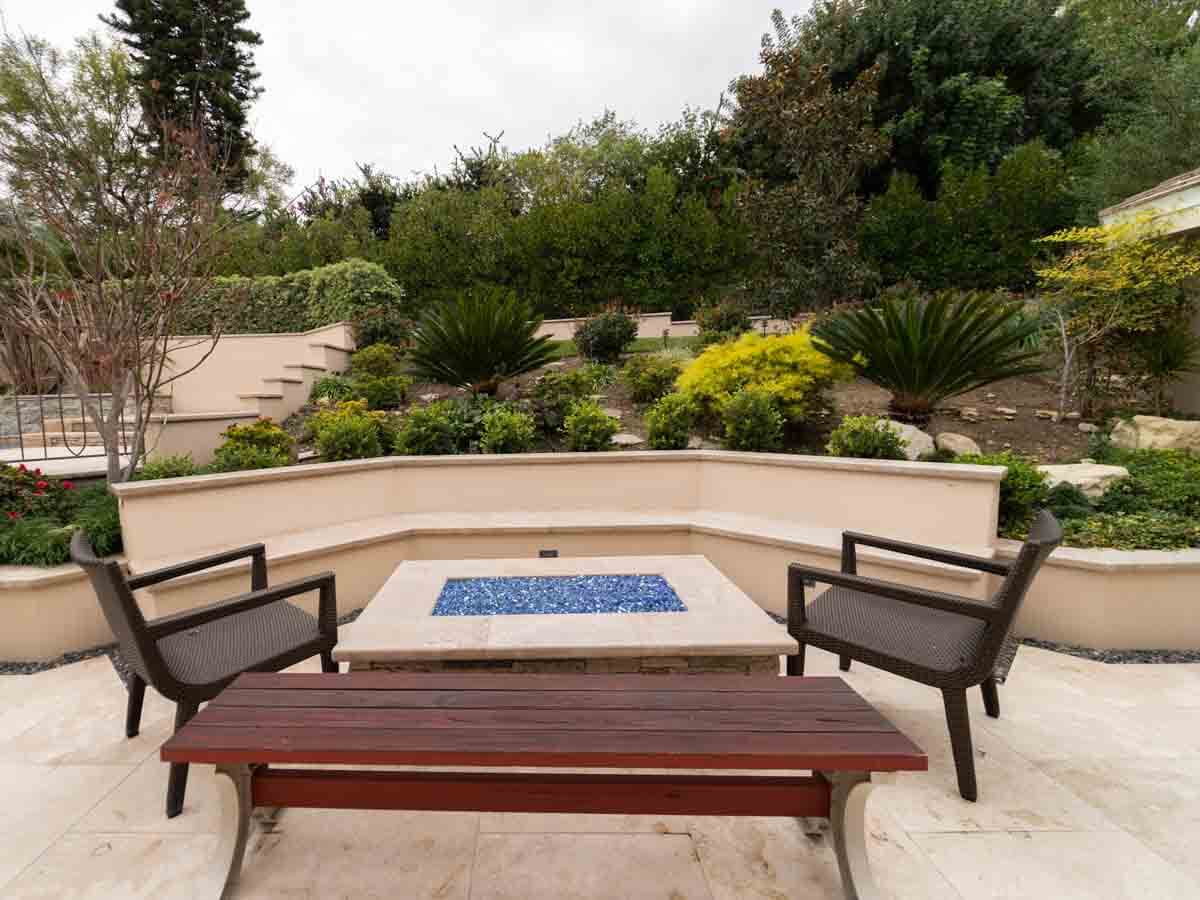 Square gas fire pit with blue fire glass wrapped by a curved seat wall and benches