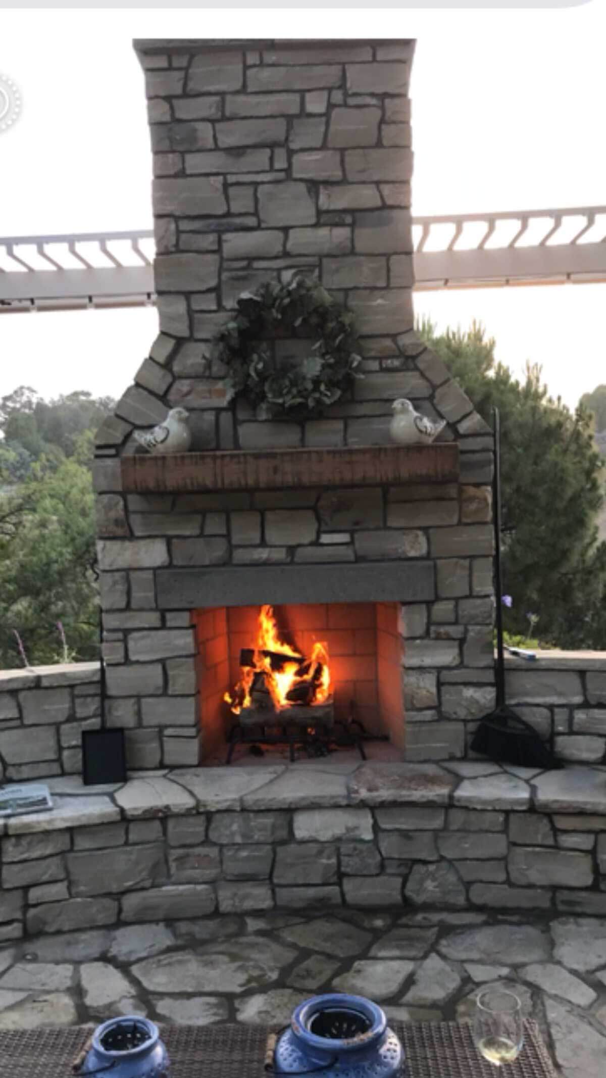 Outdoor stone fireplace lit at dusk under a pergola