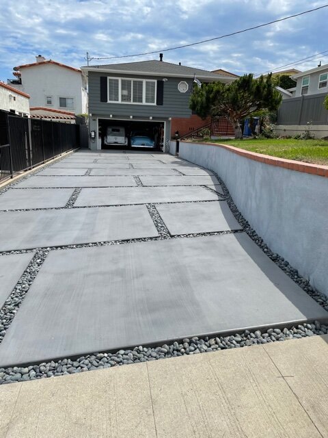 Gray concrete driveway panels separated by black pebble joints beside a brick-capped wall