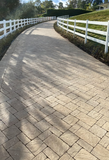 Long tumbled paver driveway along a white ranch fence