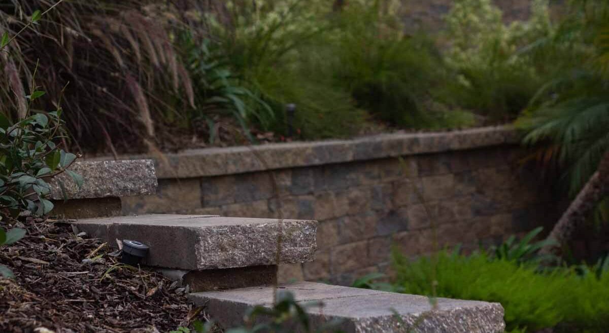 Capped block retaining wall holding back a planted hillside