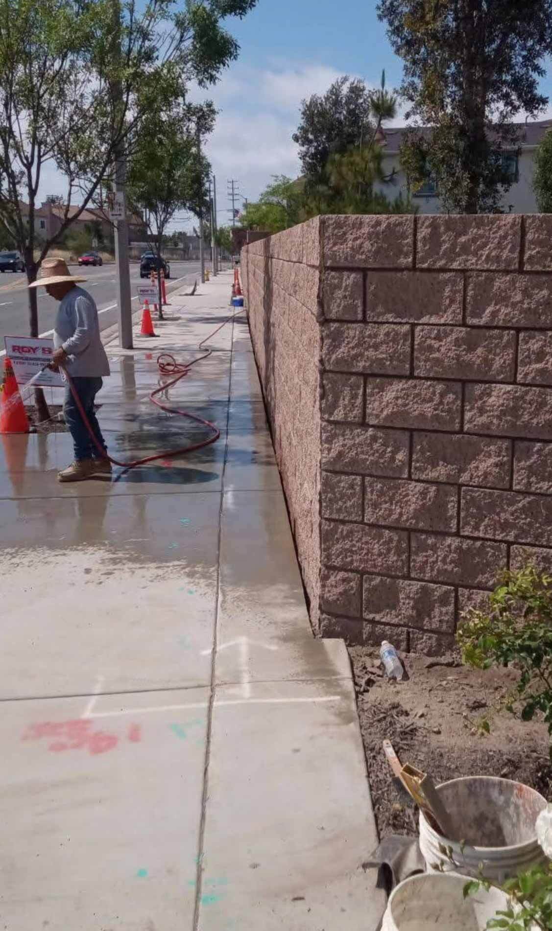 Tall freestanding split-face block wall being washed down after construction