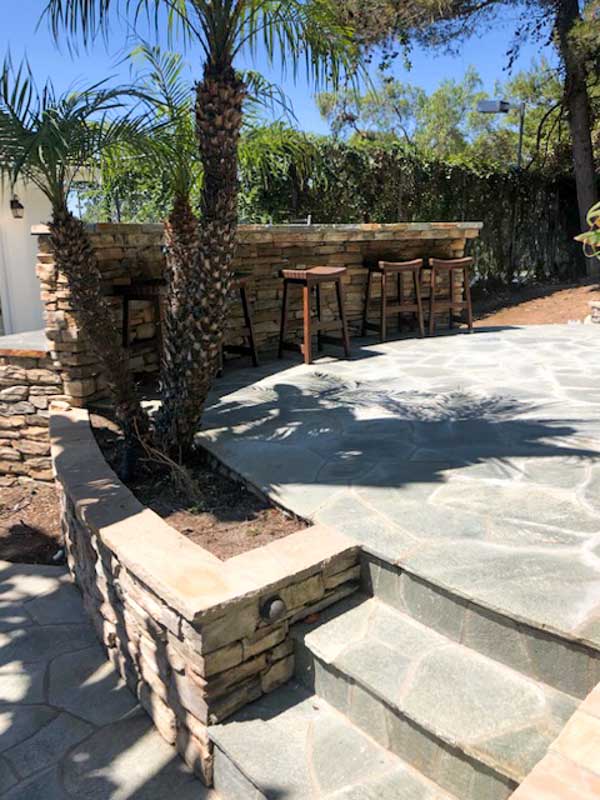 Backyard bar with stone veneer walls beside a flagstone patio and stone steps