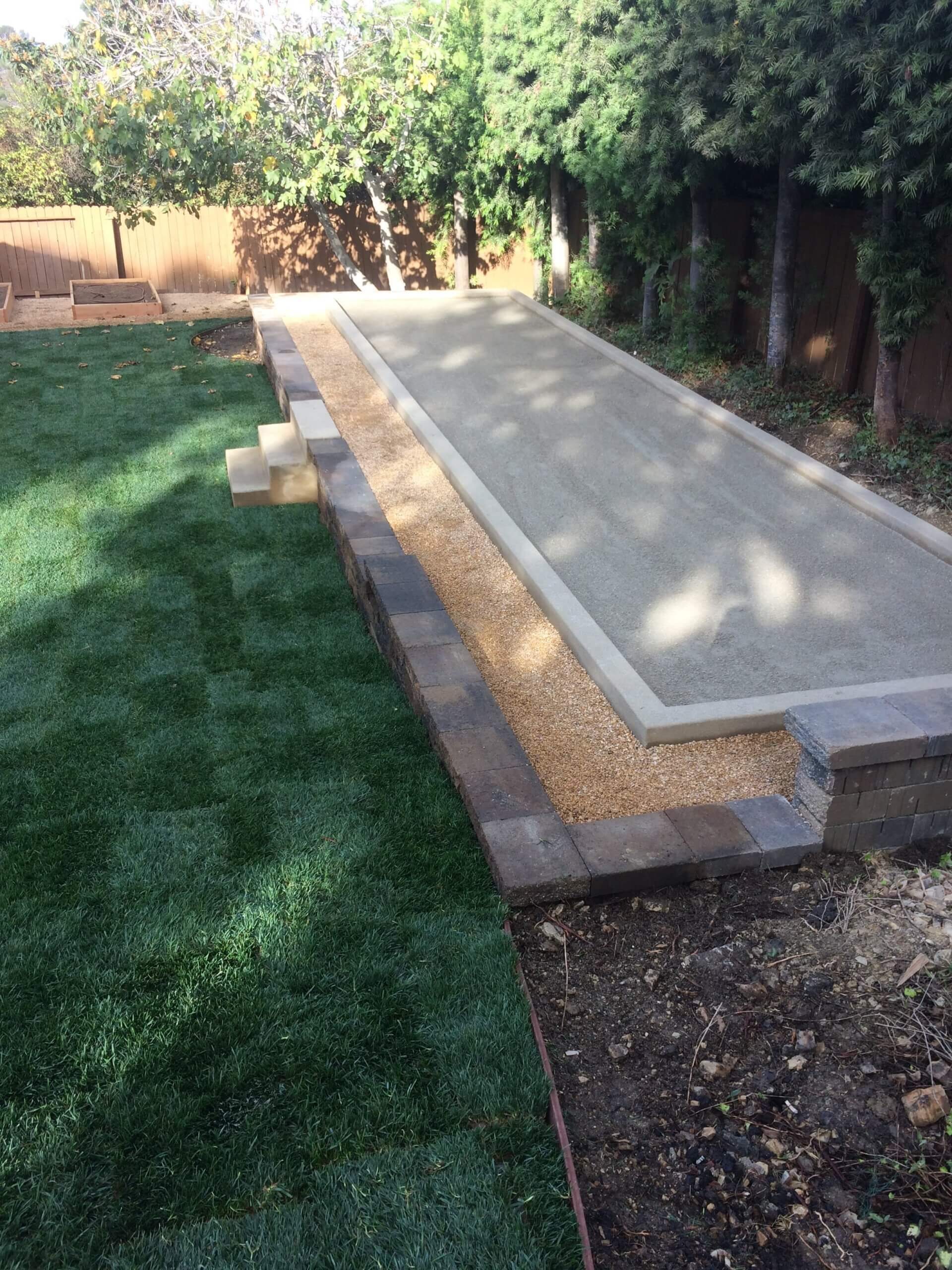 Backyard bocce court with poured concrete curbs, a gravel walk, and new turf beside it