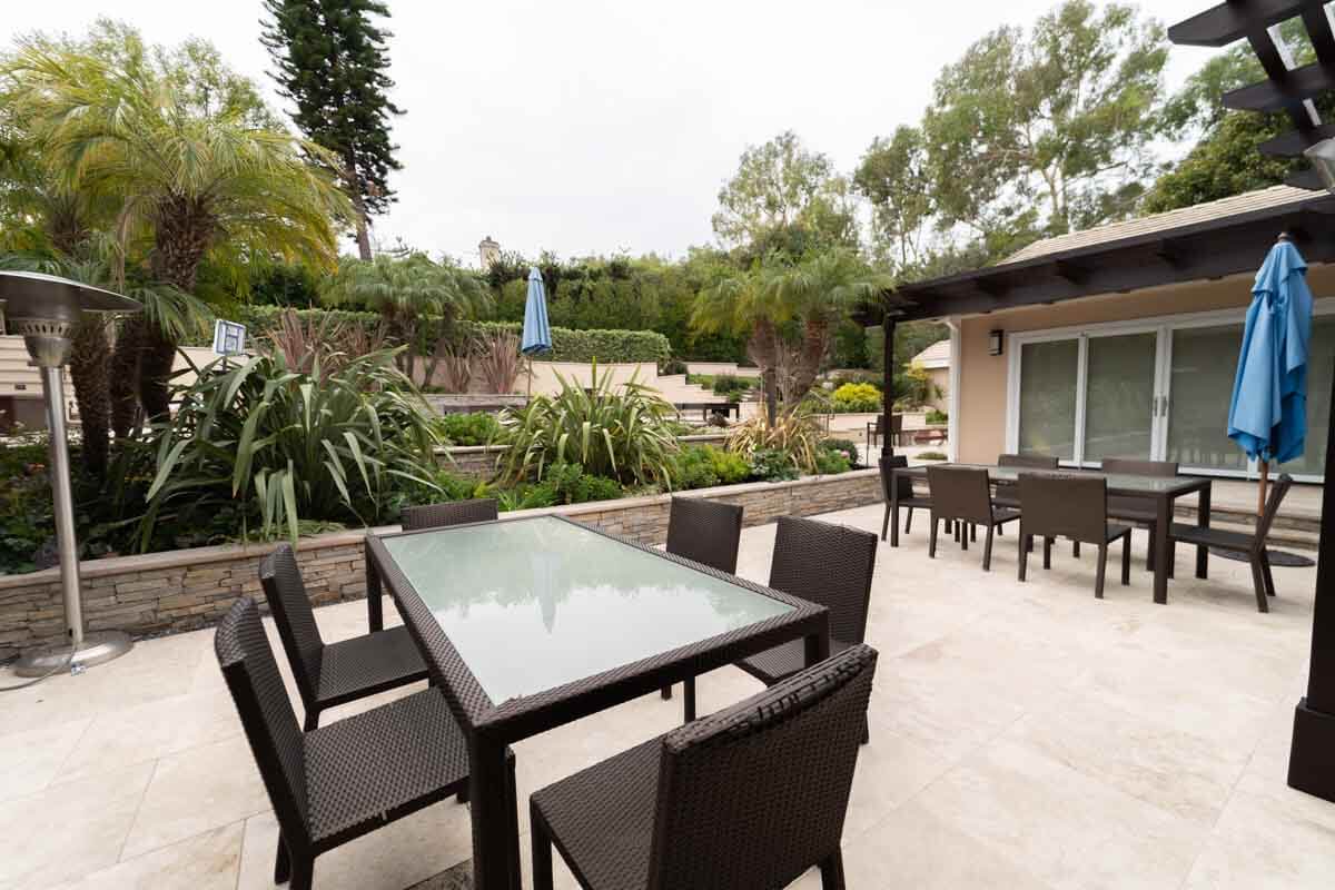 Light stone patio with two outdoor dining sets, stacked stone planter walls, and a patio heater