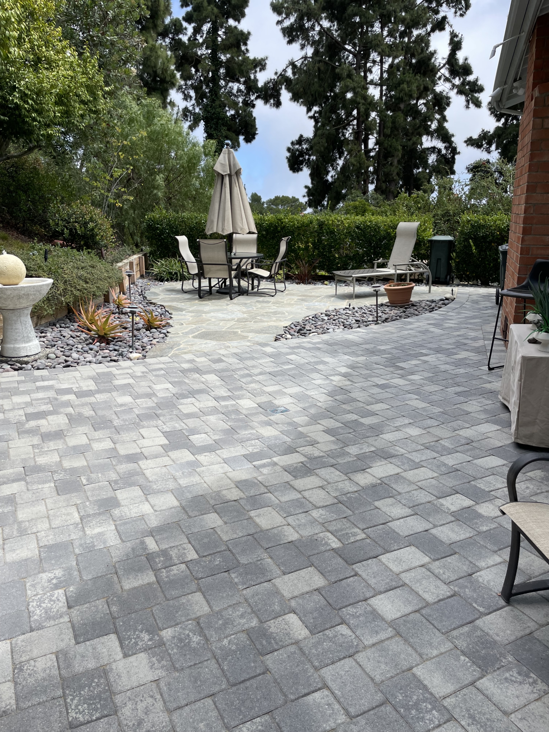 Gray interlocking paver patio with outdoor dining tables and umbrellas behind a home