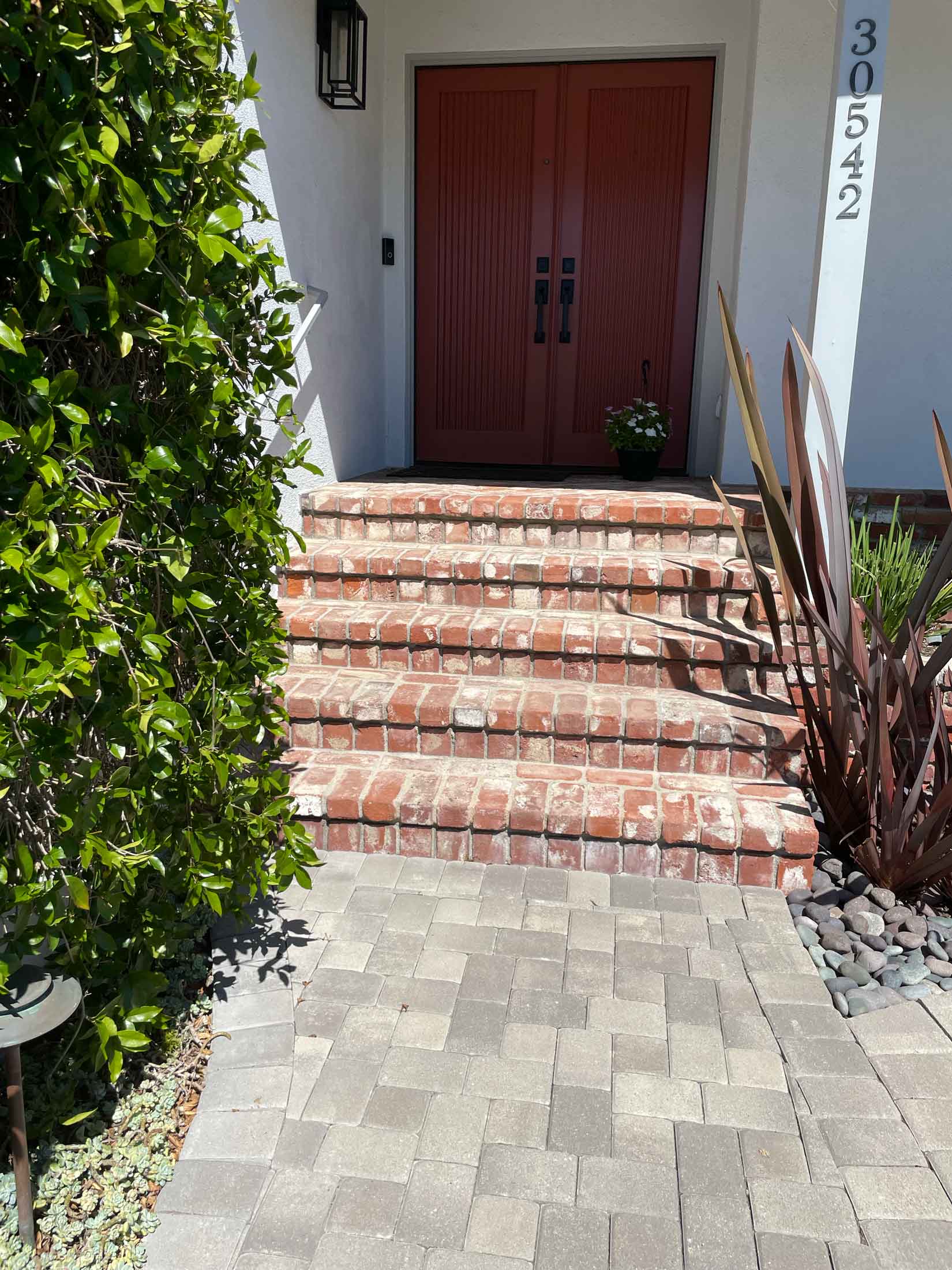Paver walkway and brick-trimmed steps leading up to red double front doors