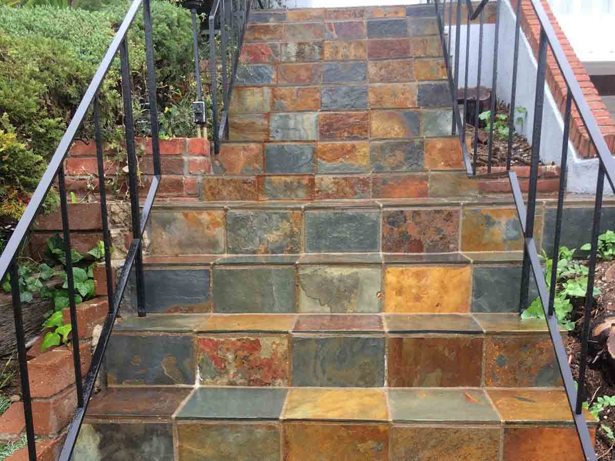 Steps tiled in multicolor slate with an iron handrail