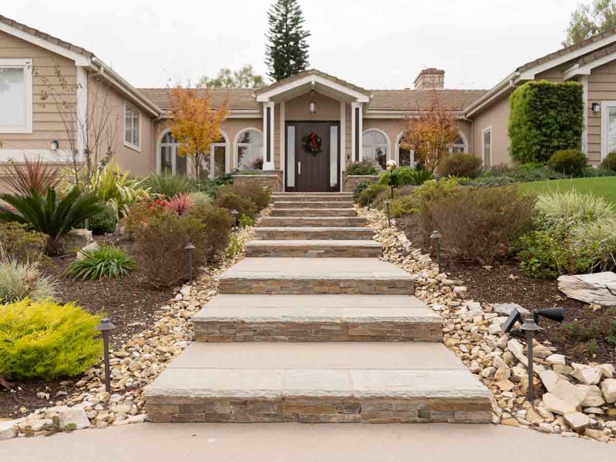 Broad front entry steps with stone-faced risers and concrete treads, edged in river rock