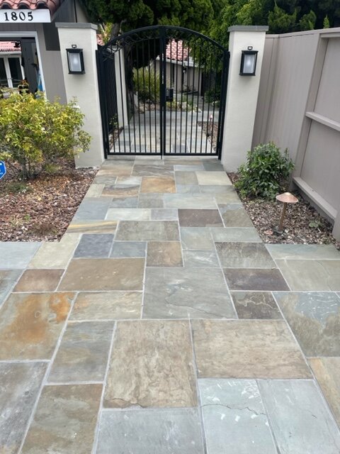 Large-format natural stone walkway leading to a gated entry with lantern pillars