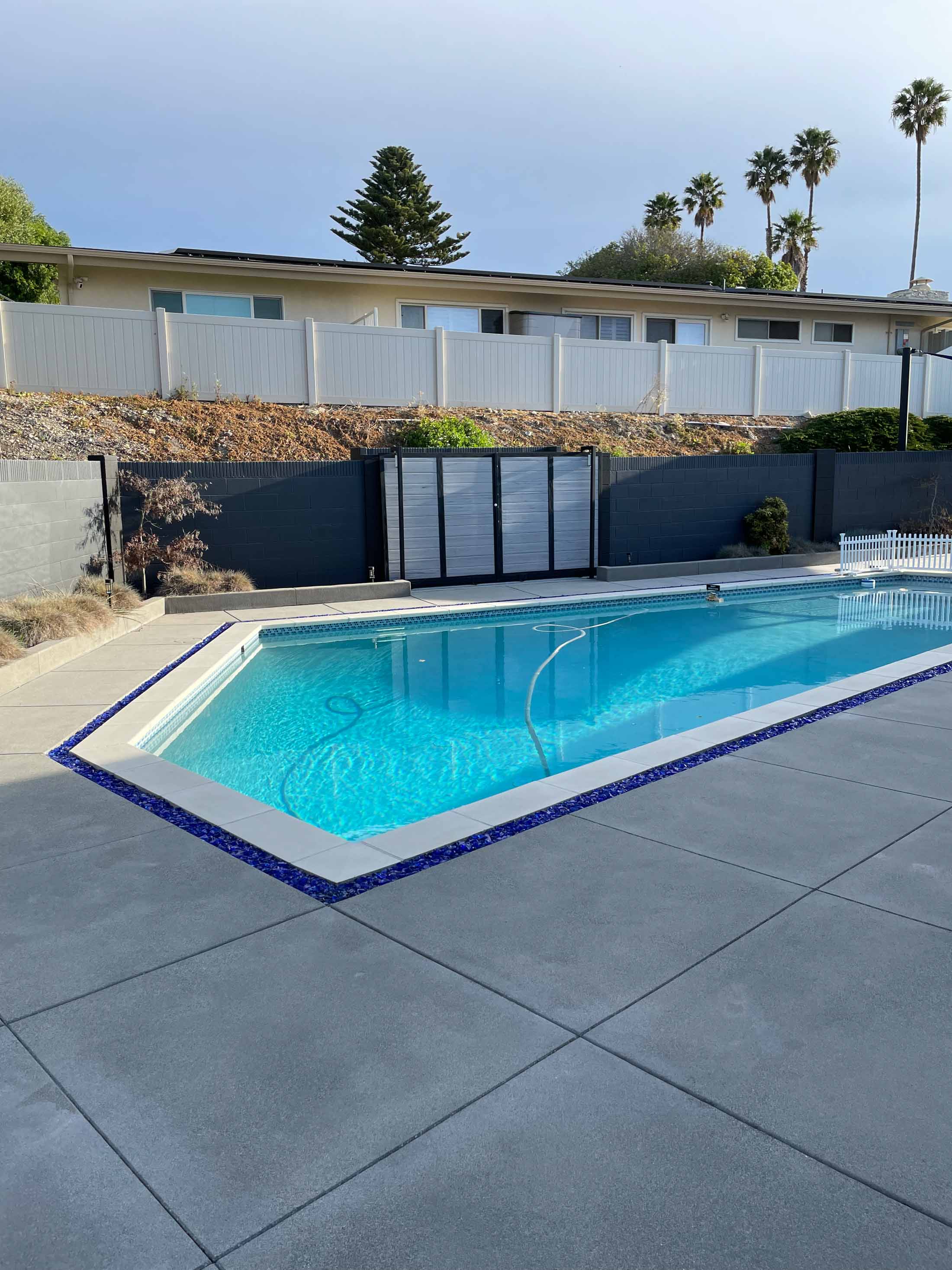 Pool with navy waterline tile and white coping surrounded by a new gray concrete deck