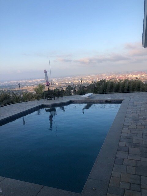 Paver pool deck at dusk with city lights in the distance