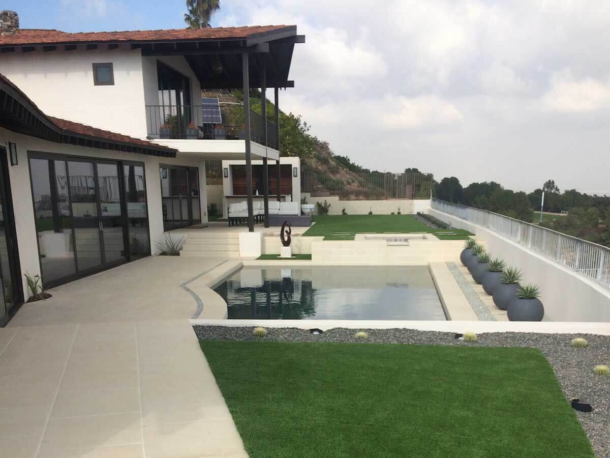 Modern white home with a new pool deck, turf panel, gravel border, and glass fencing