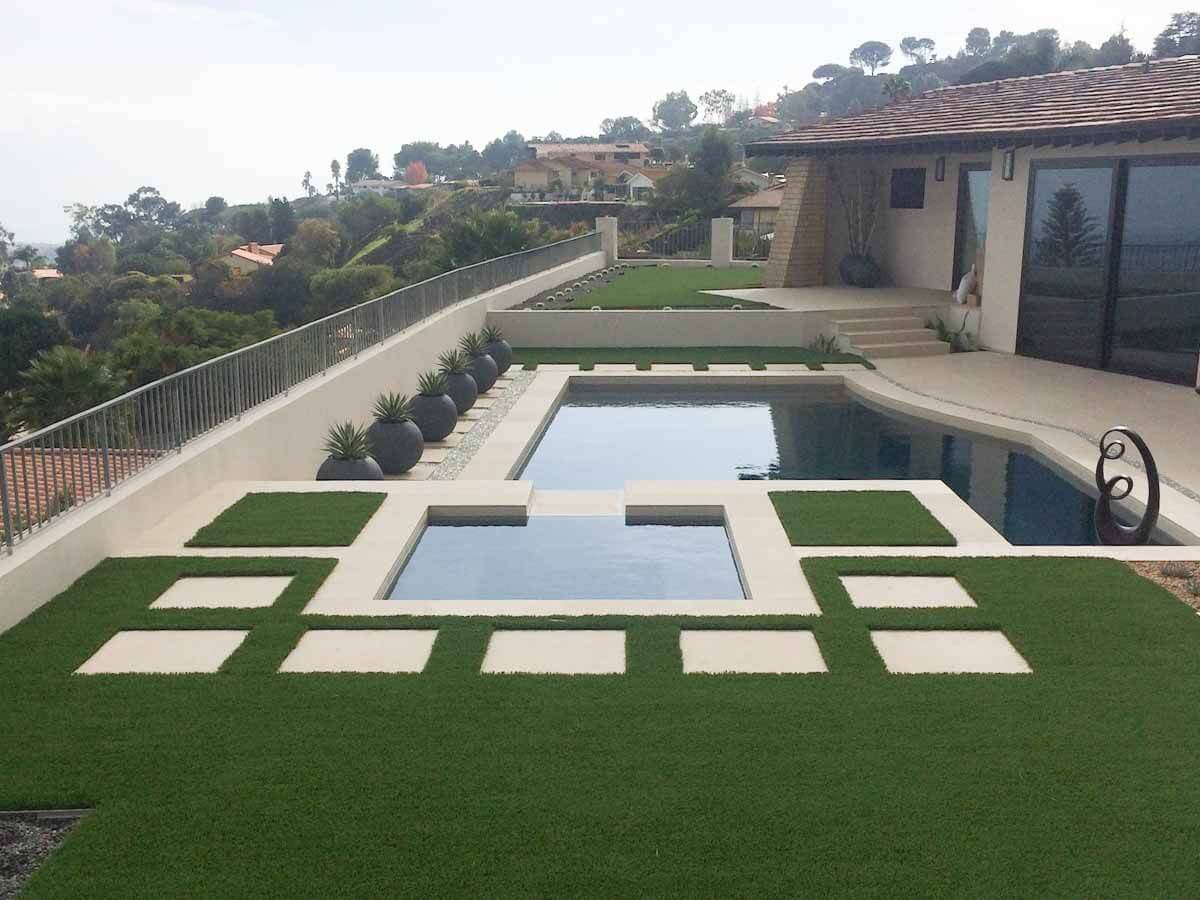 Elevated view of a modern pool and inset spa surrounded by concrete pads set in turf on a hilltop