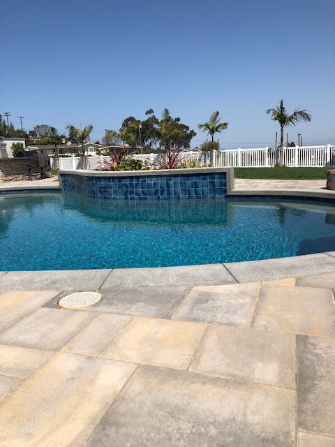 Raised spa faced in deep blue tile above a pool with a buff paver deck