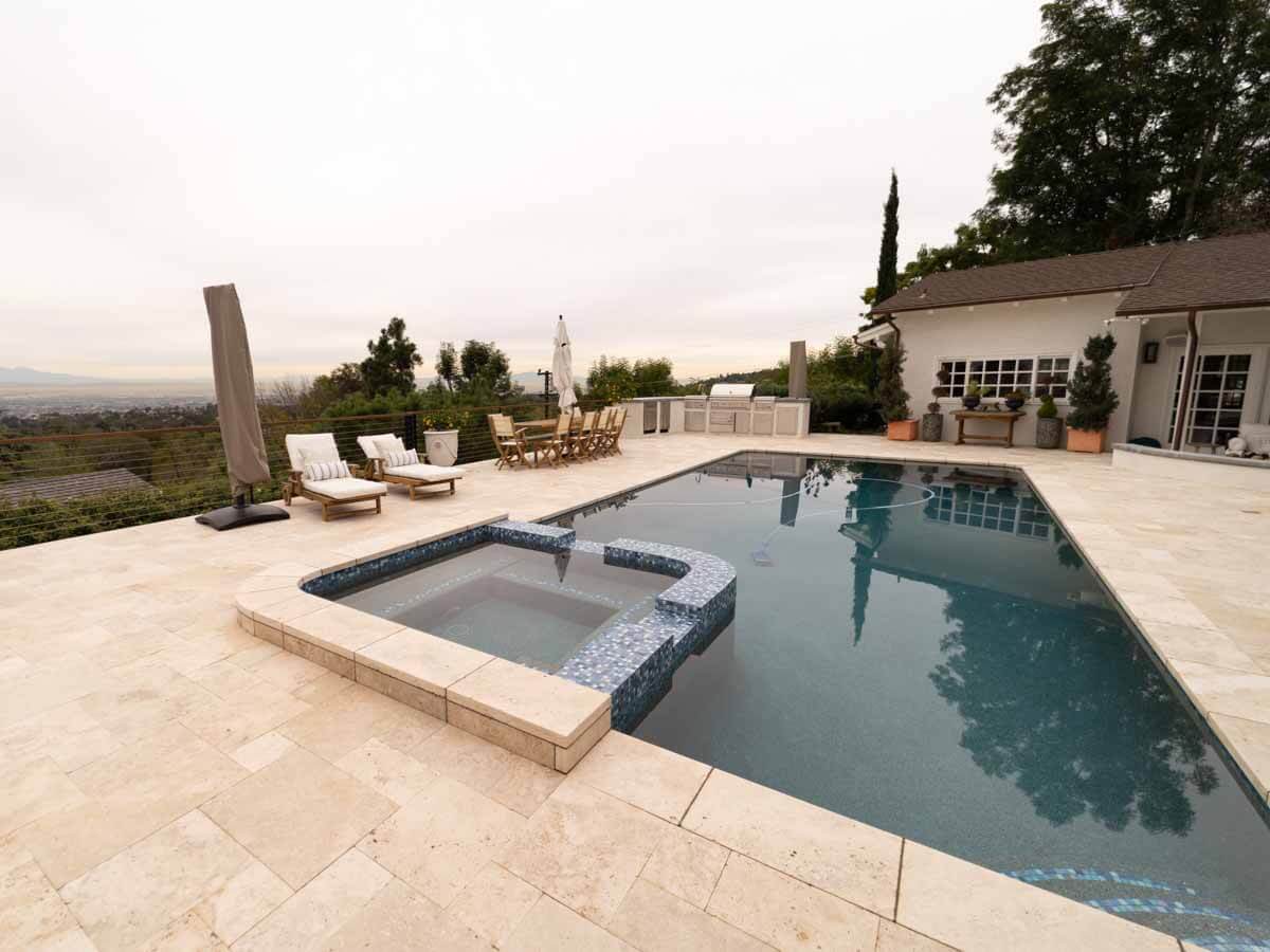 Travertine pool deck with a raised tile spa and lounge chairs overlooking the valley