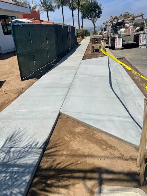 Freshly poured public sidewalk alongside a fenced construction site