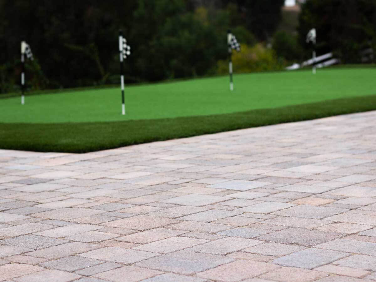 Tumbled paver patio meeting the fringe of a backyard putting green with checkered flags
