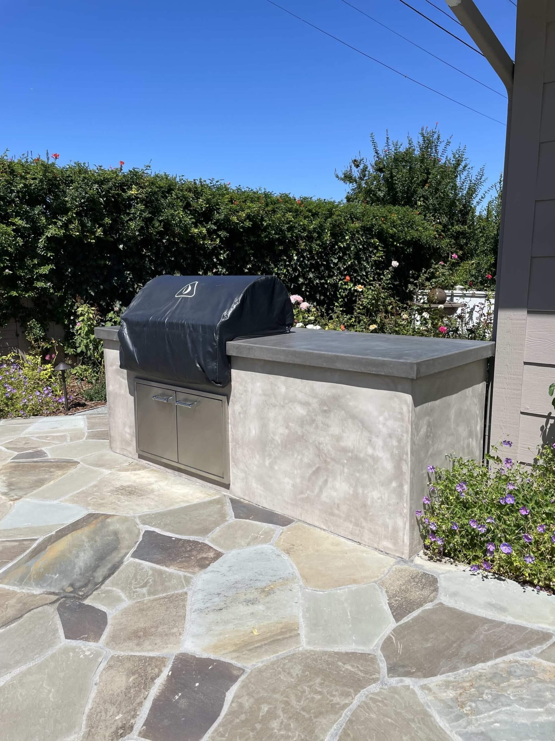 Built-in BBQ island with smooth stucco finish and poured concrete counter on a multicolor flagstone patio