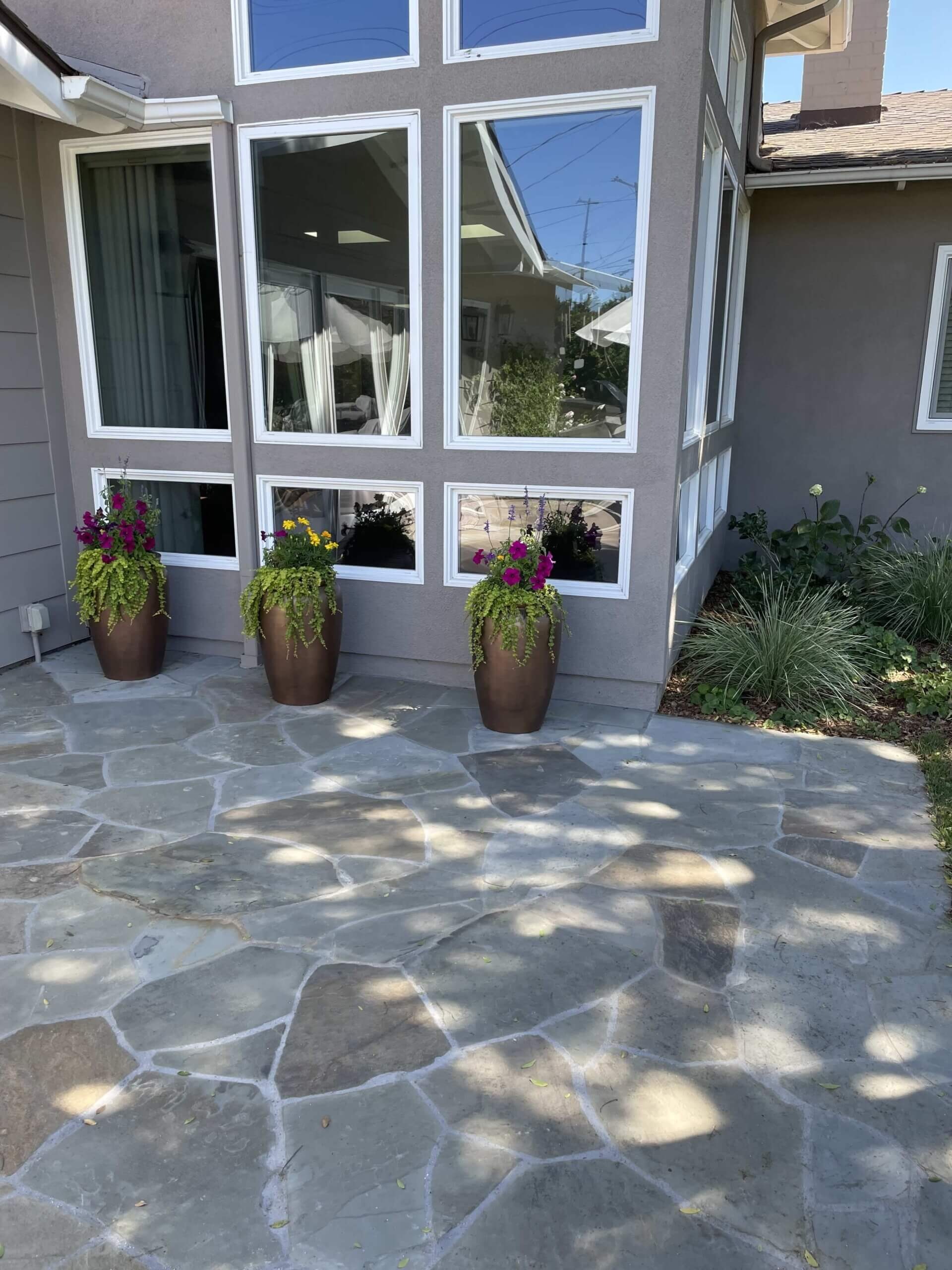 Multicolor flagstone patio beneath a bay window with potted flowers
