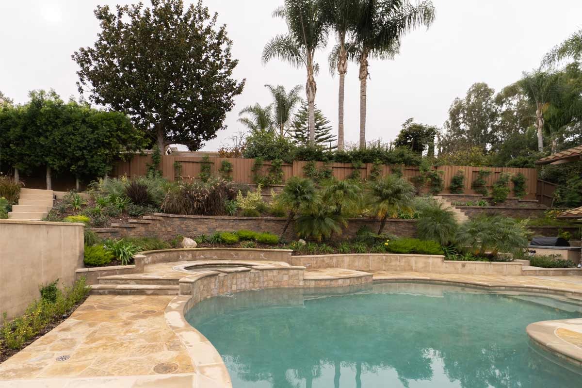 Freeform pool and raised spa wrapped in golden flagstone with terraced planting walls behind