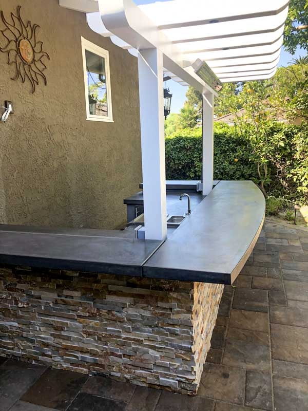 Outdoor kitchen and bar with ledger stone base, concrete countertop, and pergola