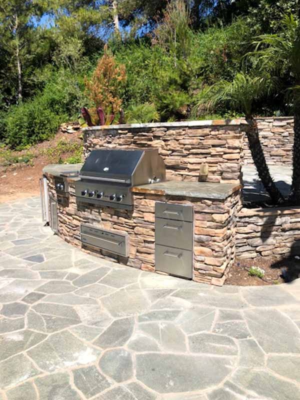 Curved outdoor BBQ island faced in stacked stone with slate paving