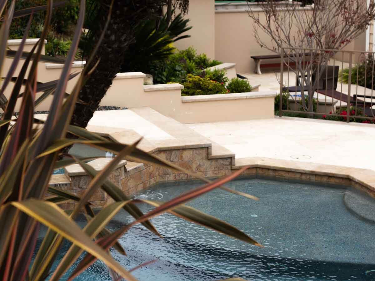 Travertine pool steps and coping with stone-tiled spa wall