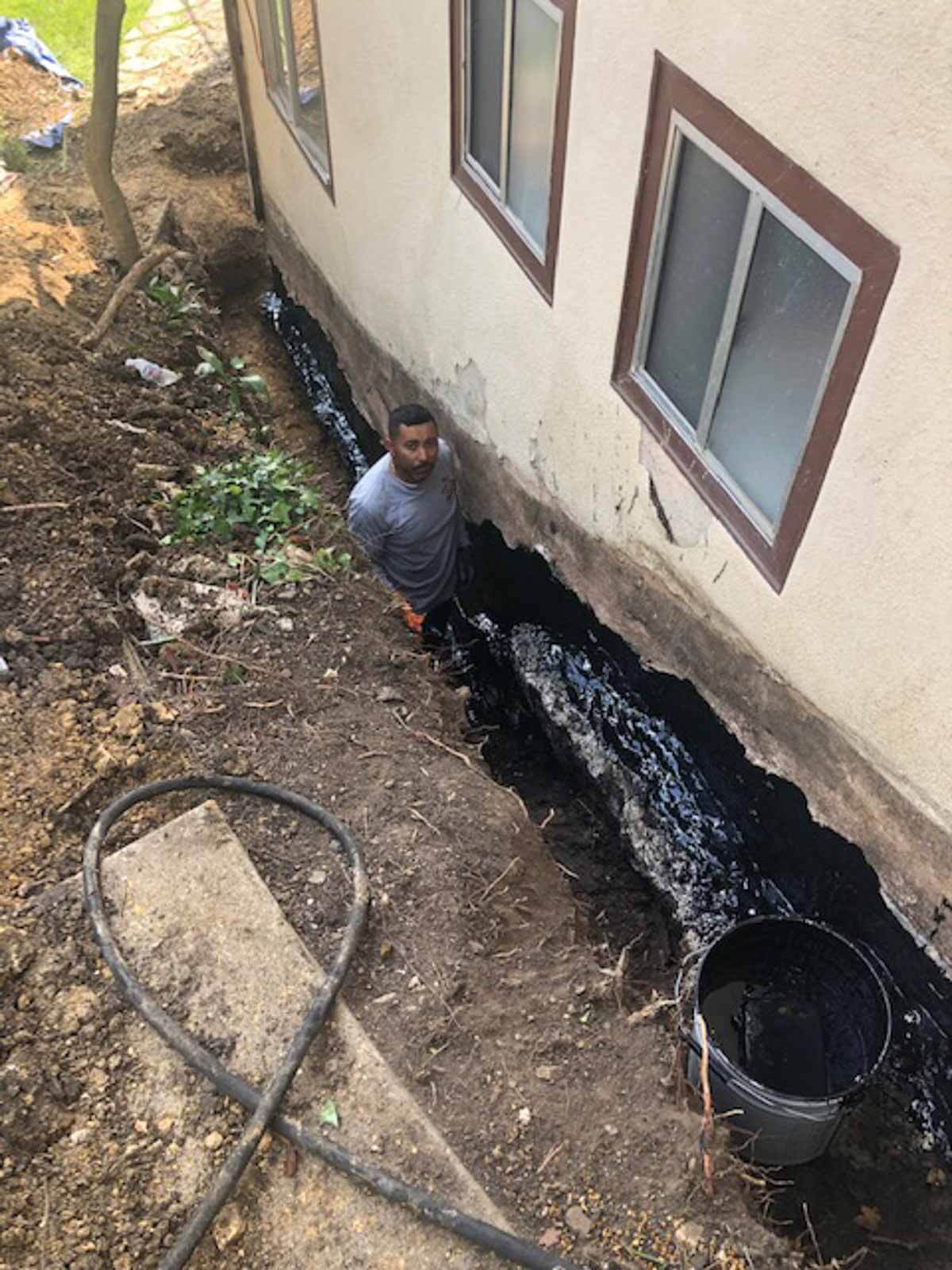 Black waterproofing membrane applied to a foundation with drainage pipe in the trench