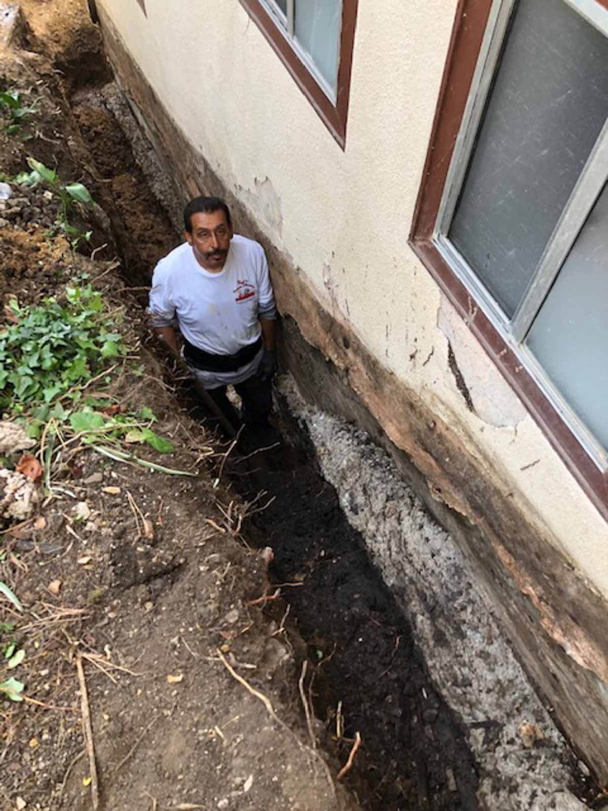 Crew member working in a trench alongside an exposed house foundation